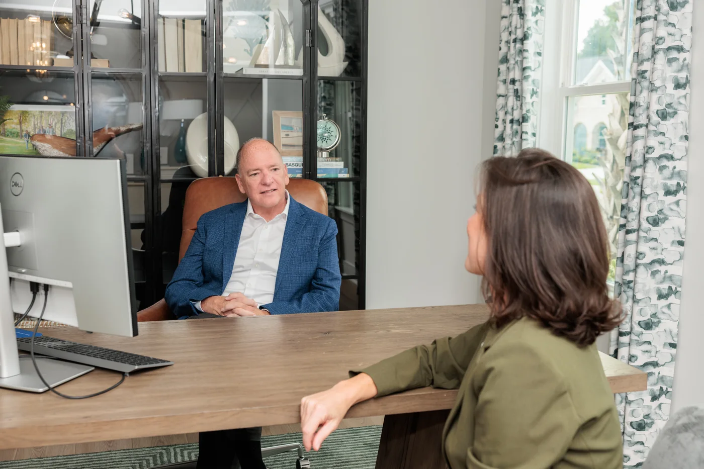 Buddy Blake talks with a woman across a desk in a bright office.